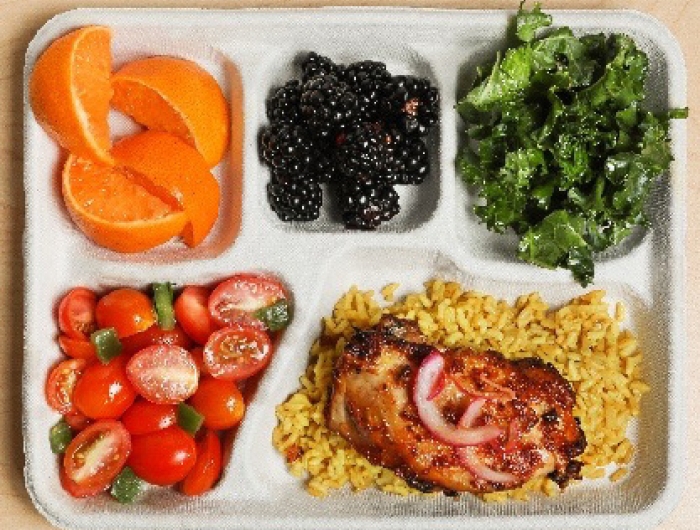 A lunch tray: orange slices, blackberries, kale salad, cherry tomato salad, and jollof rice and chicken.